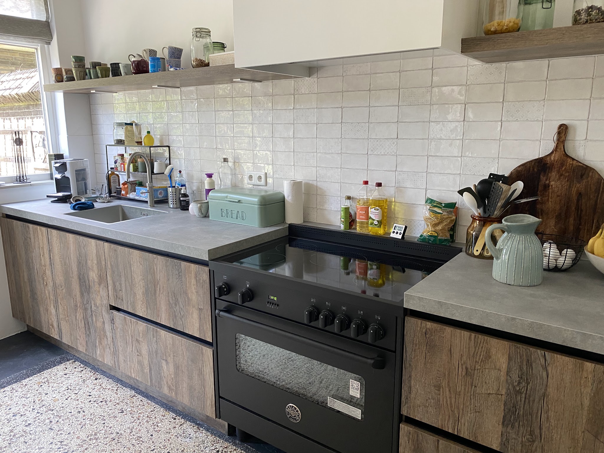 Keuken met verweerde eikenhouten fronten, betonlook werkblad, zwart fornuis en wit wandtegelwerk